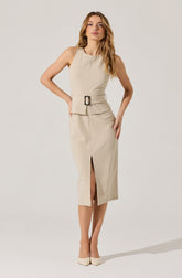 A woman is wearing a sleeveless beige dress with a fitted waist and a wide belt with a rectangular buckle. The dress features a front slit that extends below the knees. She is also wearing matching beige pointed-toe heels.